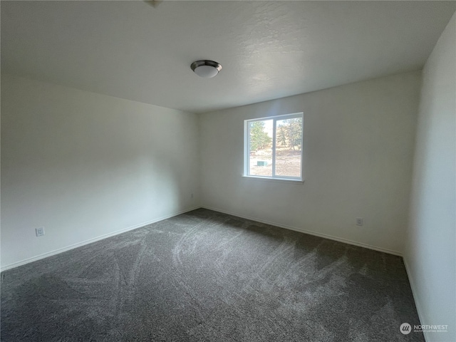 spare room featuring baseboards and dark carpet