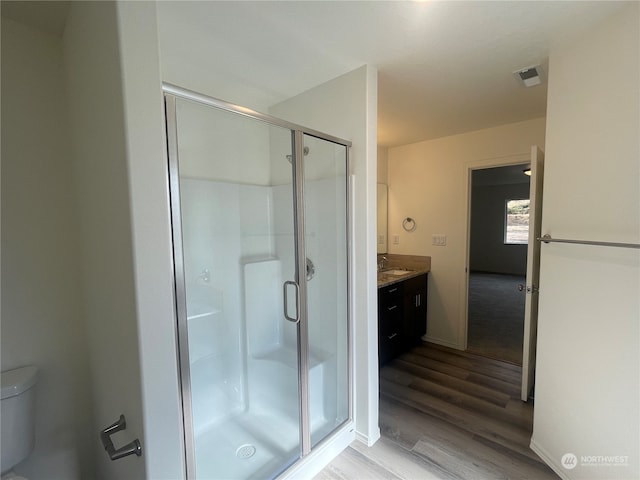 bathroom featuring wood-type flooring, vanity, a shower with shower door, and toilet