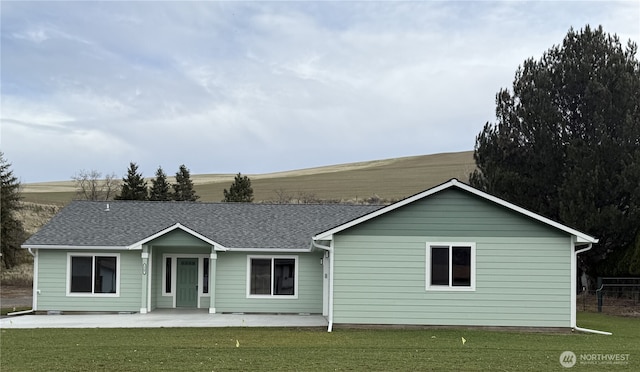 view of front facade with roof with shingles, a patio area, and a front yard