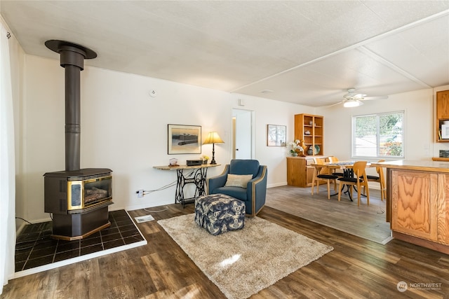 living area with dark hardwood / wood-style flooring, ceiling fan, and a wood stove