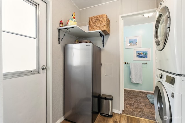 clothes washing area with stacked washer and clothes dryer, dark hardwood / wood-style floors, and wood walls