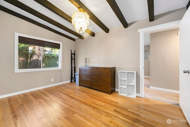 empty room featuring lofted ceiling with beams, a chandelier, and light hardwood / wood-style flooring