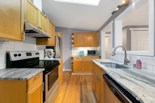 kitchen with light wood-type flooring, sink, lofted ceiling, appliances with stainless steel finishes, and light stone countertops