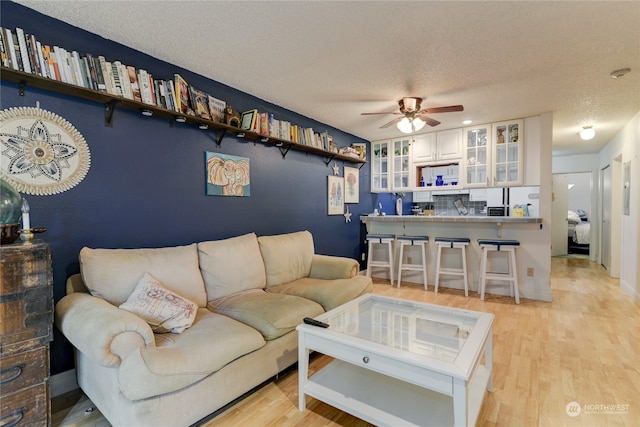 living room featuring a textured ceiling, ceiling fan, and light hardwood / wood-style flooring