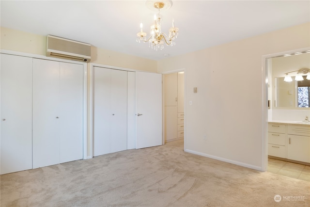 unfurnished bedroom with connected bathroom, two closets, light carpet, a notable chandelier, and a wall mounted air conditioner