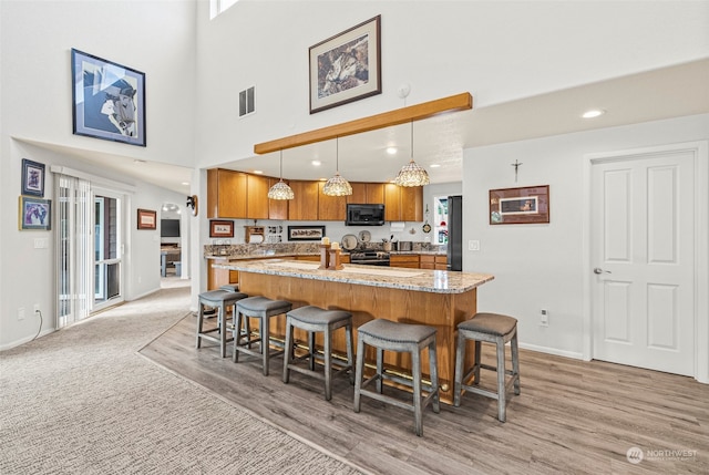 kitchen with a kitchen breakfast bar, stainless steel range oven, pendant lighting, and light hardwood / wood-style flooring