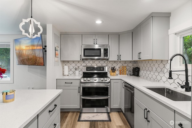 kitchen with appliances with stainless steel finishes, gray cabinets, light wood-type flooring, decorative light fixtures, and sink