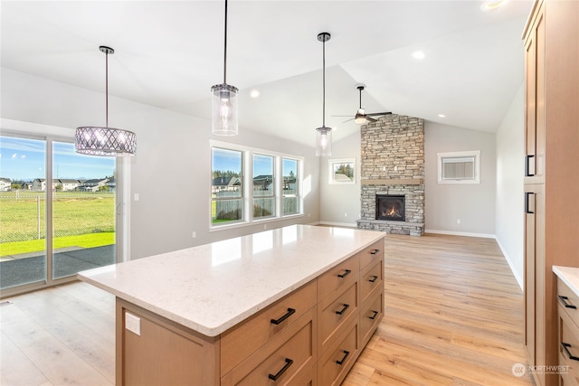 kitchen with ceiling fan with notable chandelier, a wealth of natural light, vaulted ceiling, and a stone fireplace