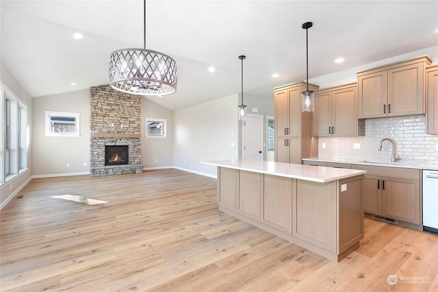 kitchen with a stone fireplace, light hardwood / wood-style flooring, vaulted ceiling, and a kitchen island