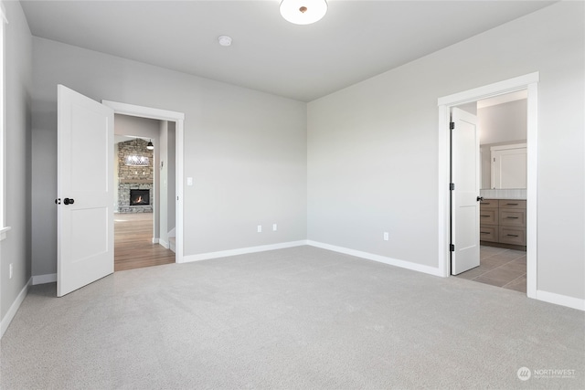 unfurnished bedroom featuring a fireplace, ensuite bathroom, and light colored carpet