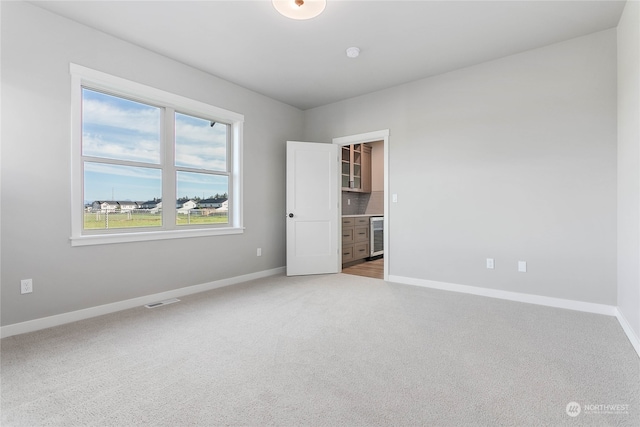 unfurnished room with beverage cooler and light colored carpet