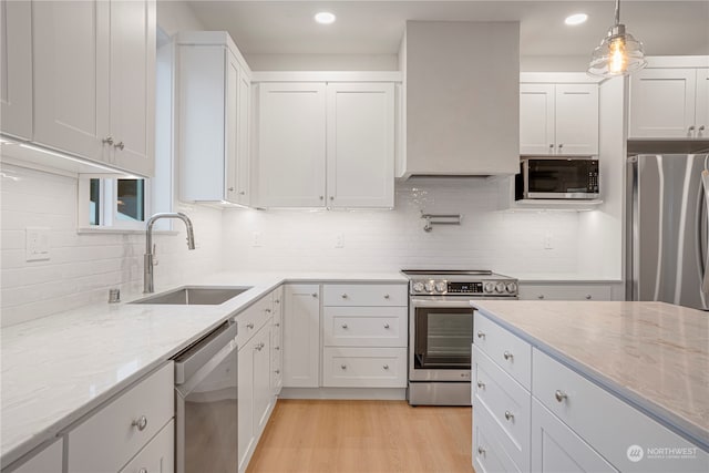 kitchen with sink, light hardwood / wood-style flooring, decorative light fixtures, white cabinets, and appliances with stainless steel finishes