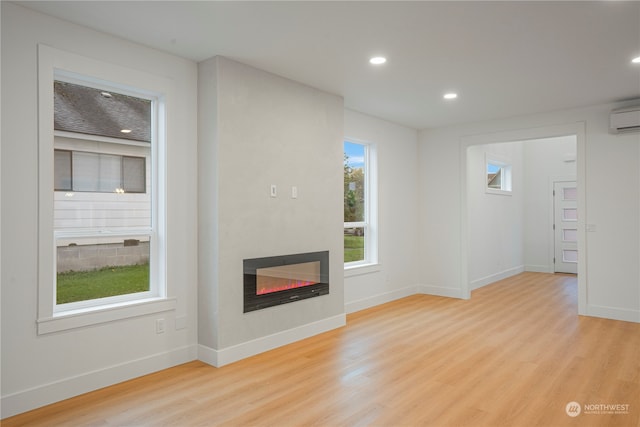 unfurnished living room with a wall mounted air conditioner, a wealth of natural light, and light hardwood / wood-style flooring