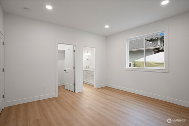 unfurnished bedroom featuring light wood-type flooring, a walk in closet, ensuite bath, and a closet