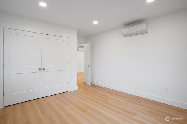 unfurnished bedroom featuring a wall mounted air conditioner, a closet, and light hardwood / wood-style flooring