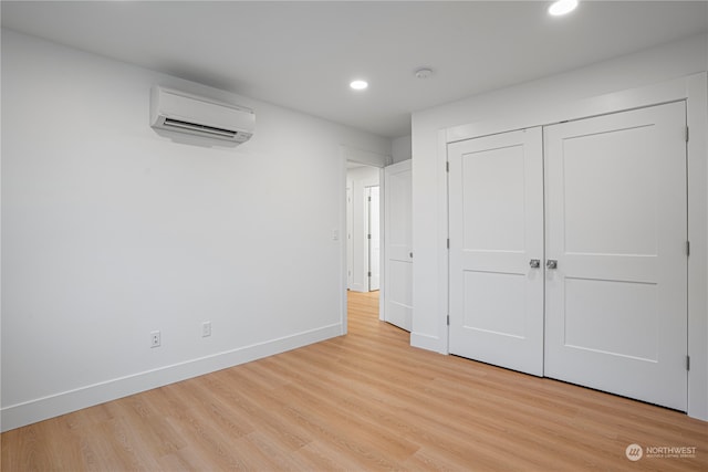 unfurnished bedroom with a closet, an AC wall unit, and light hardwood / wood-style flooring