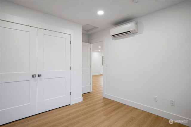 unfurnished bedroom with a wall mounted air conditioner, light hardwood / wood-style floors, and a closet