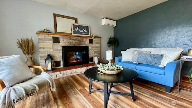 living room with a wall mounted air conditioner, hardwood / wood-style floors, and a stone fireplace