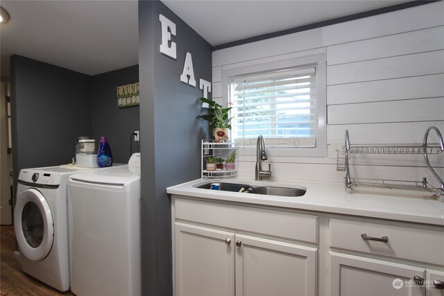 clothes washing area with dark hardwood / wood-style floors, sink, washer and dryer, and cabinets