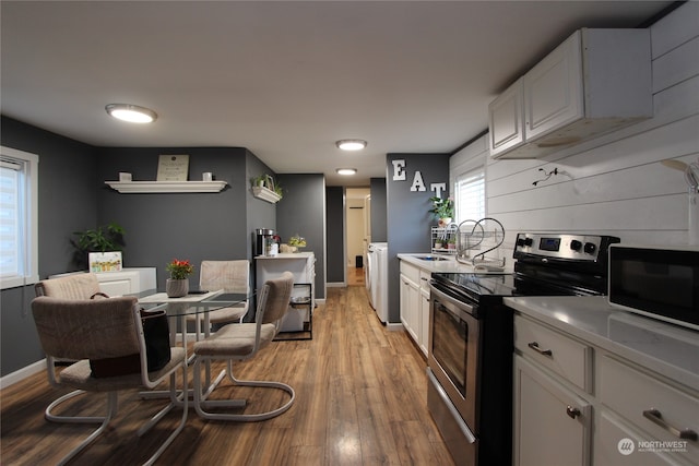 kitchen with separate washer and dryer, white cabinetry, electric range, and light hardwood / wood-style flooring