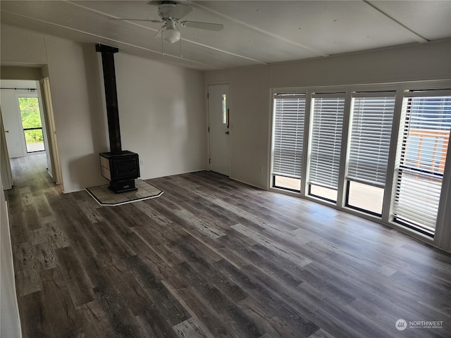 unfurnished living room featuring a wood stove, ceiling fan, and dark hardwood / wood-style flooring