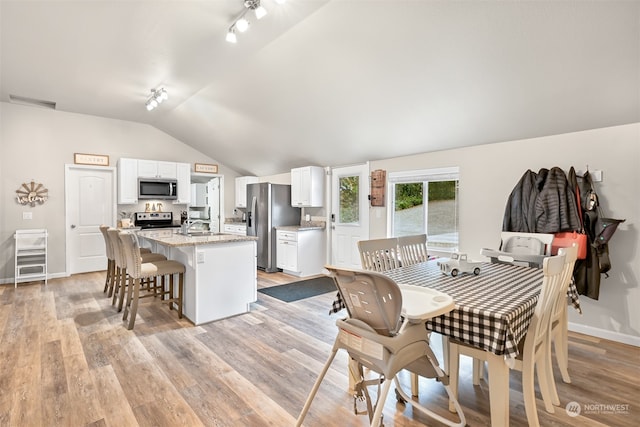 dining space with light hardwood / wood-style floors, lofted ceiling, track lighting, and sink