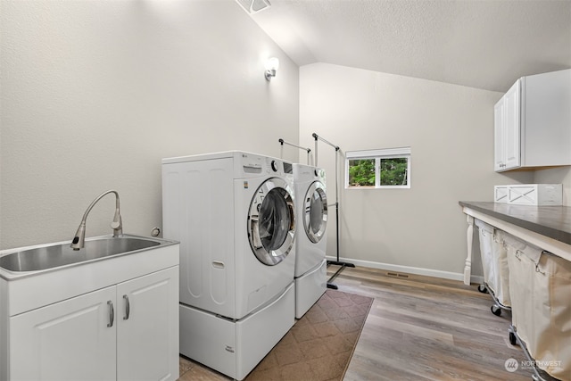 laundry area with washing machine and dryer, sink, light wood-type flooring, a textured ceiling, and cabinets