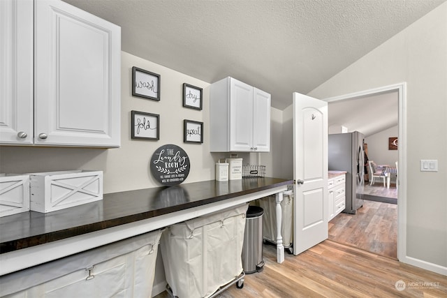 kitchen with stainless steel fridge, vaulted ceiling, light wood-type flooring, white cabinets, and a textured ceiling