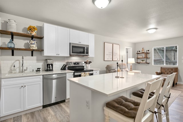 kitchen featuring white cabinets, a kitchen island, appliances with stainless steel finishes, light hardwood / wood-style flooring, and sink