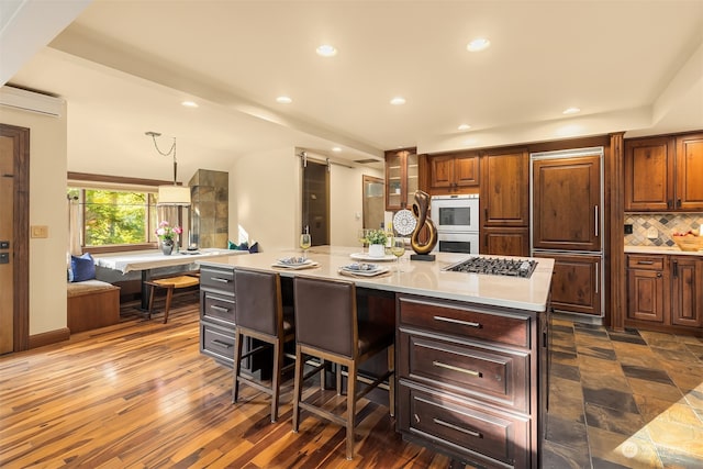 kitchen featuring decorative backsplash, dark wood-type flooring, stainless steel gas cooktop, decorative light fixtures, and a spacious island