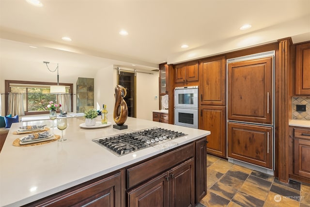 kitchen with backsplash, stainless steel gas cooktop, double oven, and hanging light fixtures