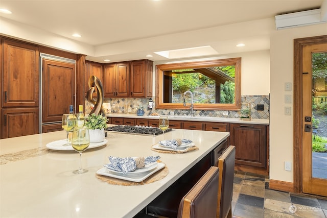 kitchen featuring an AC wall unit, a kitchen bar, backsplash, and stainless steel gas stovetop