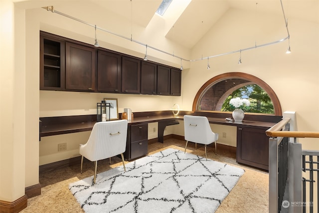 home office featuring light colored carpet, vaulted ceiling with skylight, and built in desk