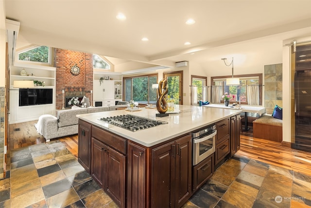 kitchen with pendant lighting, a kitchen island, appliances with stainless steel finishes, a fireplace, and vaulted ceiling