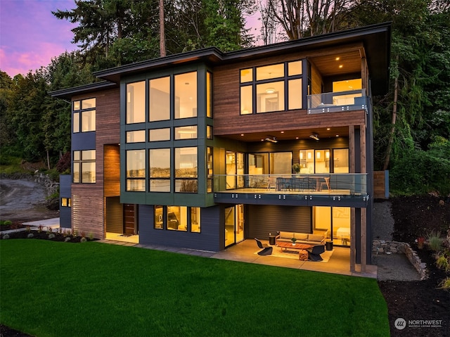 back house at dusk featuring a patio, a balcony, a lawn, and an outdoor living space