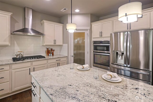 kitchen with light stone counters, dark hardwood / wood-style flooring, stainless steel appliances, decorative light fixtures, and wall chimney range hood