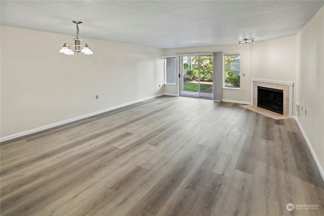 unfurnished living room featuring a textured ceiling, light hardwood / wood-style flooring, a tiled fireplace, and a notable chandelier