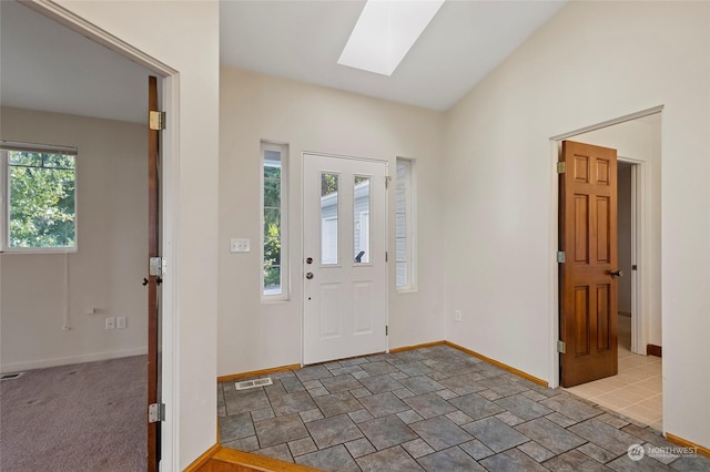 carpeted entrance foyer with baseboards, visible vents, and lofted ceiling with skylight