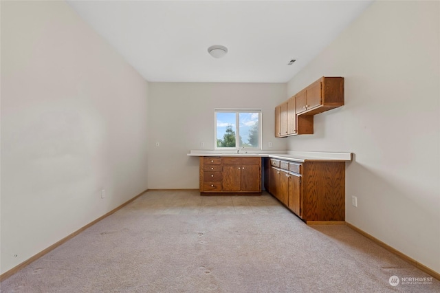 kitchen featuring baseboards, light countertops, brown cabinetry, light colored carpet, and a sink