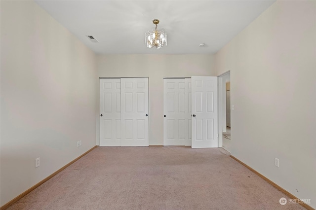 unfurnished bedroom featuring a notable chandelier, multiple closets, carpet, and baseboards