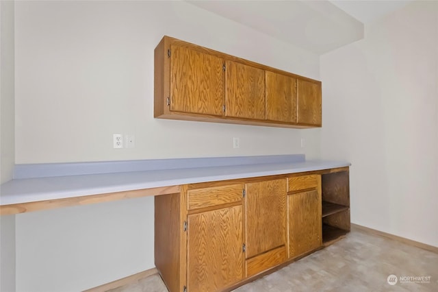 kitchen featuring brown cabinets, built in desk, and light countertops