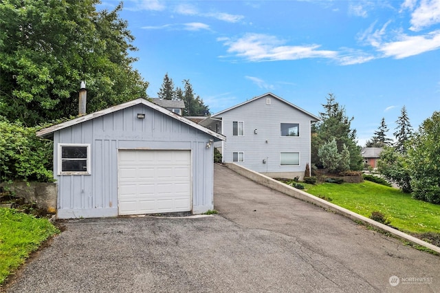 exterior space featuring a front yard, a detached garage, board and batten siding, an outdoor structure, and driveway