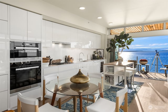 kitchen featuring a water view, sink, light hardwood / wood-style flooring, and white cabinets