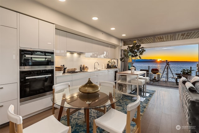 kitchen with white cabinets, sink, stainless steel gas cooktop, dark hardwood / wood-style flooring, and a water view