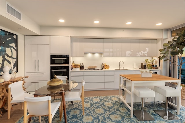 kitchen with stainless steel gas cooktop, light hardwood / wood-style flooring, black double oven, and white cabinetry