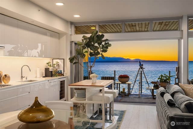 interior space featuring light hardwood / wood-style floors, a water view, sink, and wine cooler