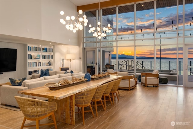 dining area with light wood-type flooring, a notable chandelier, a towering ceiling, a water view, and expansive windows