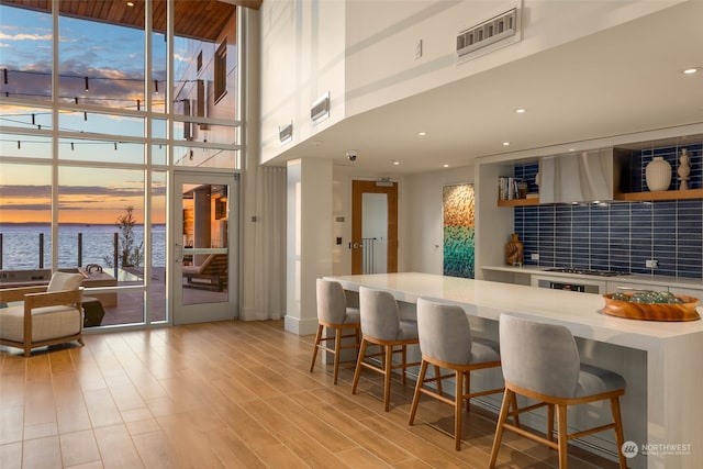 kitchen with ventilation hood, a kitchen breakfast bar, a water view, and light hardwood / wood-style flooring