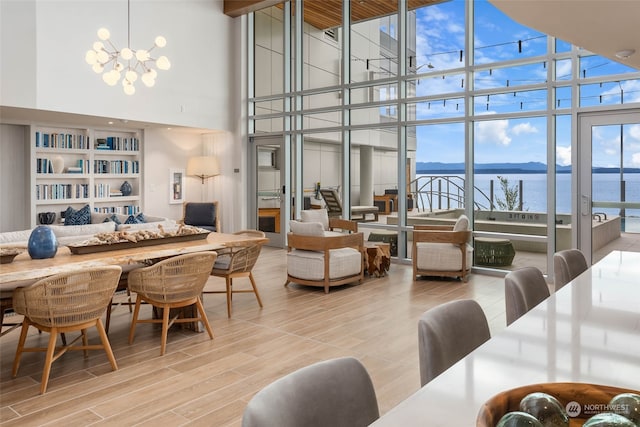 dining area with a water view, a towering ceiling, expansive windows, an inviting chandelier, and hardwood / wood-style floors