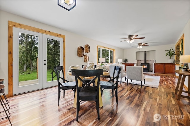 dining area featuring ceiling fan, a wood stove, wood-type flooring, and a healthy amount of sunlight